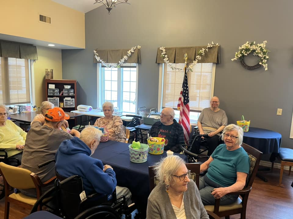 A group of people in a room, sitting around tables with decorations and an American flag, creating a cheerful atmosphere.