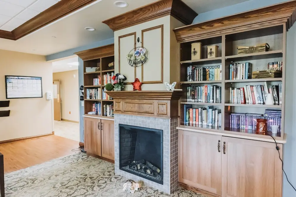 Cozy living room with a stone fireplace flanked by built-in wooden bookcases, a decorative mantel with a wreath, and a patterned area rug.
